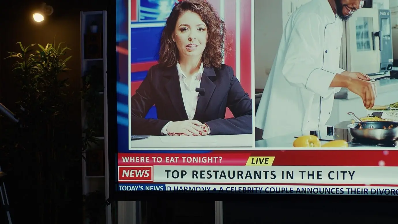 Домашний кинотеатр с большим современным телевизором, настроенным на новостной канал, в квартире, украшенной комнатными растениями.